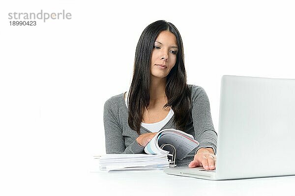 Serious Young Attractive Woman Scanning eine Mappe während der Forschung an ihrem Laptopcomputer auf dem Schreibtisch. vor weißem Hintergrund