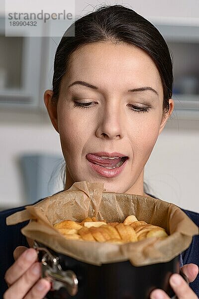 Glückliche junge Köchin  die einen frisch gebackenen Apfelkuchen oder eine Torte in der Hand hält  die sie gerade in einer Backform aus dem Ofen genommen hat  während sie das Dessert für das Abendessen vorbereitet