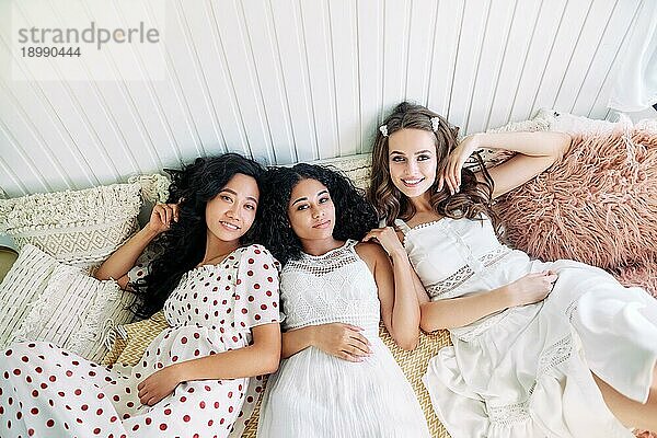 Schöne Multi ethnische Mädchen haben Spaß zusammen  entspannen und liegen auf dem Bett im Inneren des Wohnmobils. Frauen Freundschaft und Frauen Schönheit Konzept. Kaukasisch  afrikanisch amerikanischen und asiatischen Mädchen posieren bei Licht Innen