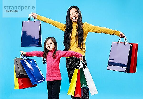 Glückliche Mutter mit entzückenden kleinen Tochter hält Einkaufstaschen genießen ihren Kauf auf blauem Hintergrund. Spaß  Verkauf  Familie Konzept
