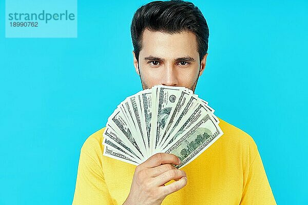 Glücklicher junger Mann hält einen Stapel Geld und prahlt mit seinen Ersparnissen auf blauem Hintergrund. Geschäft  Einkommen  Erfolg Konzept