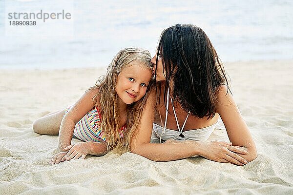 Junge schöne Frau küsst ihre kleine Tochter entspannen am tropischen Strand im Sommerurlaub. glückliche Familie  Liebe Konzept