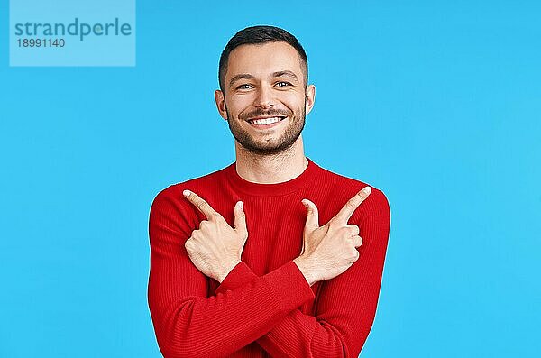 Gutaussehender  glücklicher Mann  der mit seinen Fingern auf leeren Kopierraum zeigt  vorblauem Hintergrund. Präsentiert Produkt und Werbekonzept