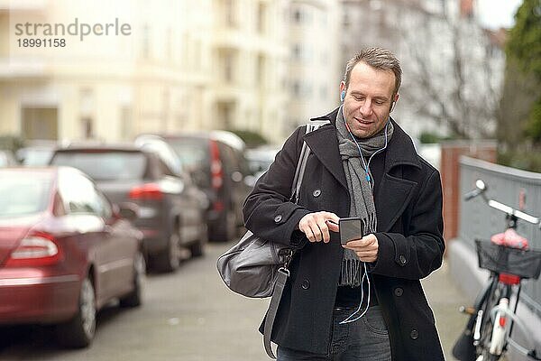 Attraktiver Mann in Wintermode  der auf einer städtischen Straße steht und sein Mobiltelefon auf Nachrichten überprüft oder einen Anruf tätigt  Nahaufnahme des Oberkörpers