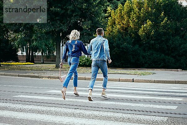 Rückansicht eines jungen glücklichen Paares  das auf der Straße über den Zebrastreifen läuft. Spaß  Wandern  Dating Konzept