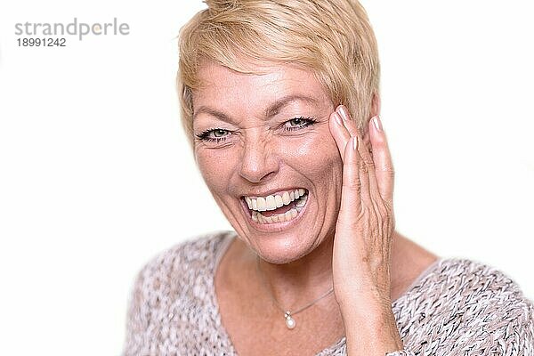 Nahaufnahme Glückliche Frau mittleren Alters mit kurzen blonden Haaren  lachend  während sie ihr Gesicht berührt und in die Kamera schaut