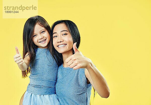 Glückliche Mutter und ihr Kind Tochter zeigt Daumen hoch und haben Spaß zusammen auf gelbem Hintergrund. Familie  Motivation Konzept