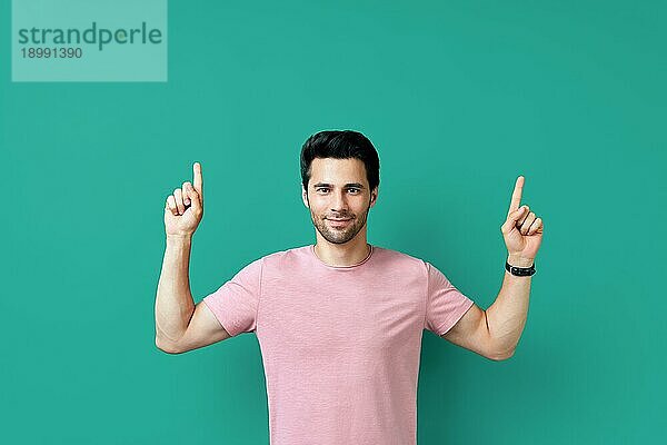 Gutaussehender  glücklicher Mann zeigt mit dem Finger auf leeren Kopierraum  vorblauem Hintergrund. Präsentiert Produkt und Werbekonzept