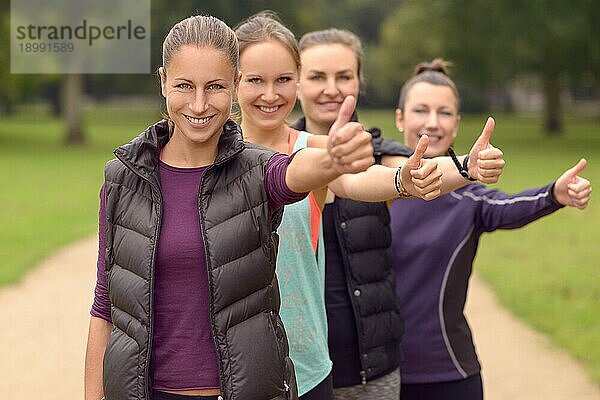 Vier glückliche  gesunde junge Frauen in der Schlange  die nach ihrer Outdoor Übung den Daumen in die Kamera halten