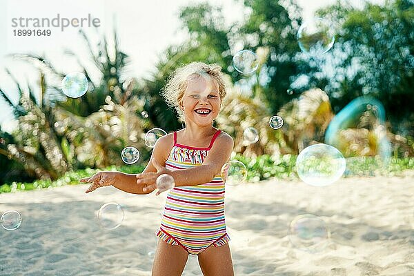 Kleines glückliches Mädchen spielt Seifenblasen am aktuellen Strand. Kindheit  LifestyleKonzept