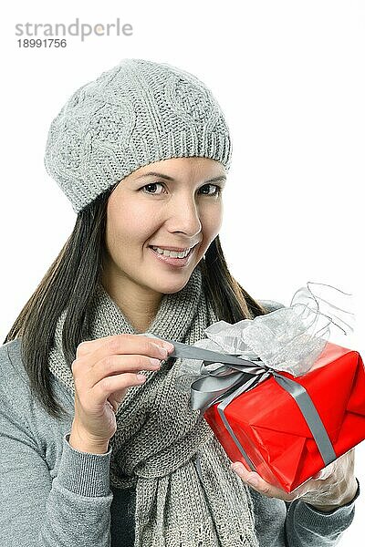 Close up Hübsche lächelnde junge Frau in Wintermode hält Geschenkbox während Blick auf Kamera  vor weißem Hintergrund