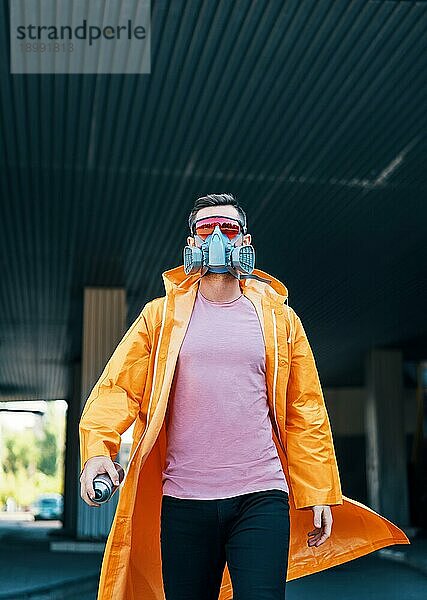 Trendiger junger Mann mit Atemschutzmaske geht die Straße entlang und schaut in die Kamera