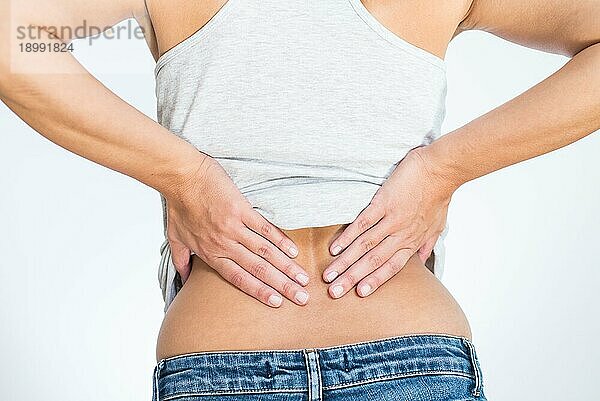 Rückansicht einer Frau mit Schmerzen im unteren Rücken  die sich mit den Händen an Rücken und Wirbelsäule festhält  um den Schmerz in den Muskeln oder in den Wirbeln und Bandscheiben zu lindern  der durch Stress  Verletzungen oder Krankheiten verursacht wird