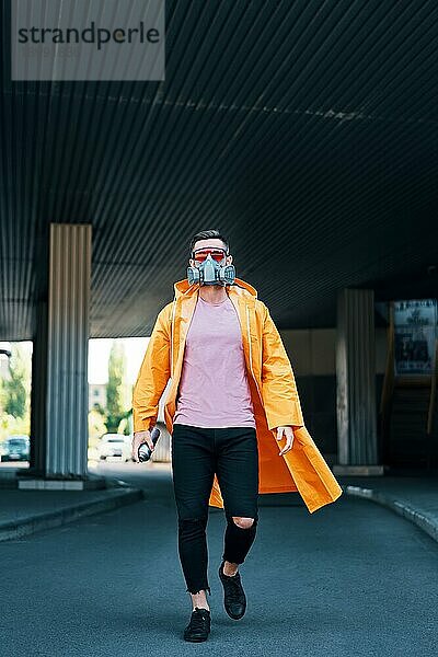 Trendiger junger Mann mit Atemschutzmaske geht die Straße entlang und schaut in die Kamera