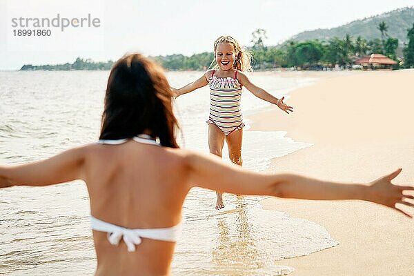 Glückliches kleines Mädchen läuft zu ihrer Mutter für Umarmungen am tropischen Strand. Sommerurlaub  glückliche Familie  Liebe Konzept