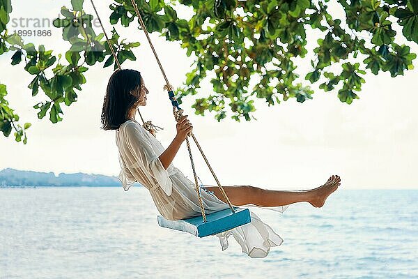 Sorglose glückliche Frau auf einer Schaukel an einem paradiesischen Strand. Entspannung und Freiheit Konzept