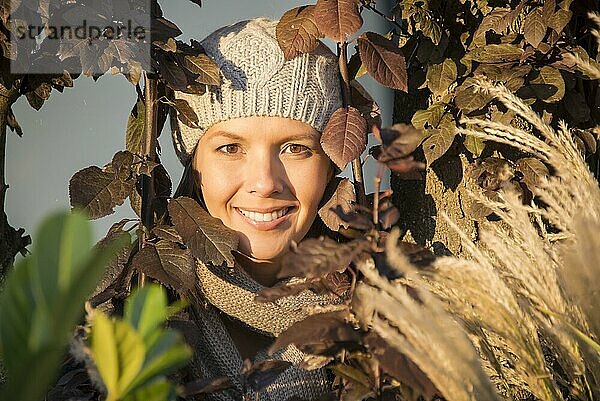 Schöne Frau  die eine warme Wollmütze trägt  steht lächelnd in der Herbstsonne und genießt einen Tag des späten indischen Sommers während des Wechsels der Jahreszeiten