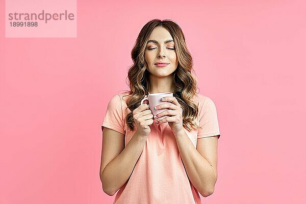 Junge hübsche Frau genießt Tasse Kaffee Aroma geschlossen Augen auf rosa Hintergrund. Entspannen und ausruhen Konzept