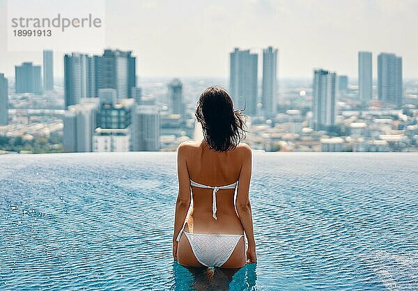 Junge schöne Frau entspannen im Schwimmbad auf dem Dach und genießen Stadtbild. Sommerurlaub Konzept