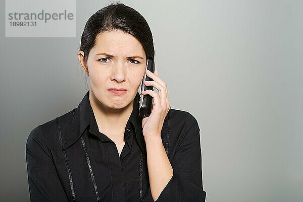 Attraktive Frau  die mit einem traurigen Gesichtsausdruck einem Gespräch über ihr Handy oder Smartphone zuhört  während sie in die Kamera schaut