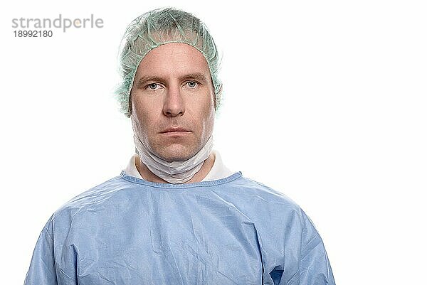 Freundlicher Krankenpfleger oder Arzt in OP Kleidung  der einen OP Kittel  eine Maske  eine Schutzbrille und eine Kappe trägt und direkt in die Kamera schaut  Kopf und Schultern vor weißem Hintergrund