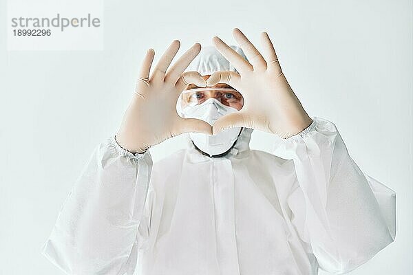 Arzt macht Herzformsymbol mit Händen tragen schützenden medizinischen Anzug auf weißem Hintergrund