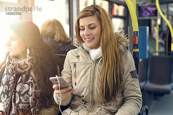 Glückliche blonde Frau  die eine Nachricht auf ihrem Mobiltelefon liest  während sie in einem Bus sitzt  öffentlicher Verkehr und Technologiekonzept