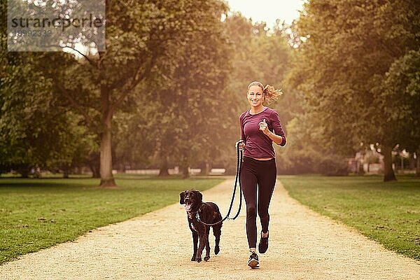 Totale Aufnahme einer gesunden jungen Frau beim Joggen im Park mit ihrem schwarzen Hund