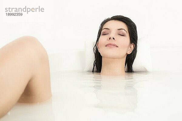 Glückselige schöne junge Frau  die sich in einem heißen Bad verwöhnt  wobei nur ihr Gesicht über dem Seifenwasser zu sehen ist  während sie sich mit heiterem Gesichtsausdruck und geschlossenen Augen entspannt