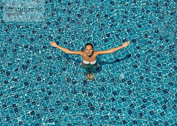 Draufsicht auf eine glückliche Frau  die die Arme zur Sonne hebt und sich im Schwimmbad entspannt. Sommerurlaub Konzept