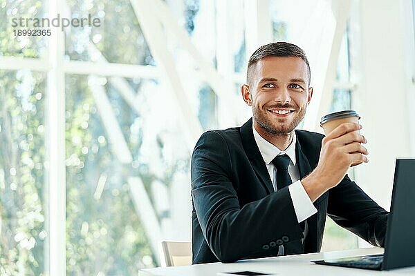 Glücklich gut aussehend Geschäftsmann entspannen mit einer Tasse Kaffee in der Hand während der Pause in einem modernen Büro mit Kopie Raum. Ruhe  Erfolg Konzept