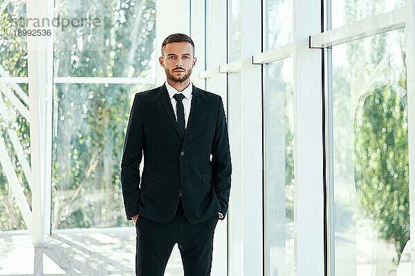 Selbstbewusster Geschäftsmann in elegantem Anzug posiert in einem modernen  kreativen Büro. Menschen im Geschäft