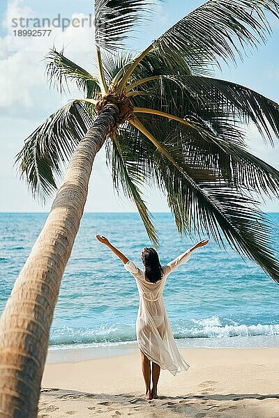 Rückansicht einer glücklichen jungen Frau  die ihren tropischen Strandurlaub unter einer Palme genießt. Sommer Konzept