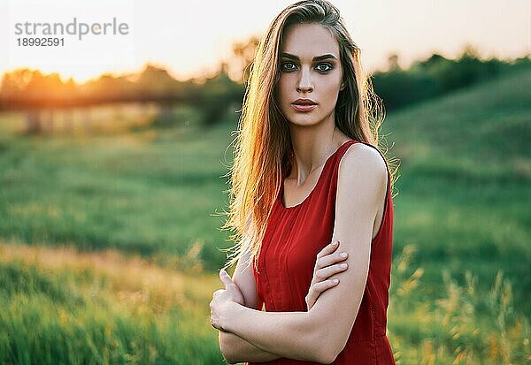 Porträt einer schönen  selbstbewussten jungen Frau mit verschränkten Armen  die in der Sommersonne im Freien posiert