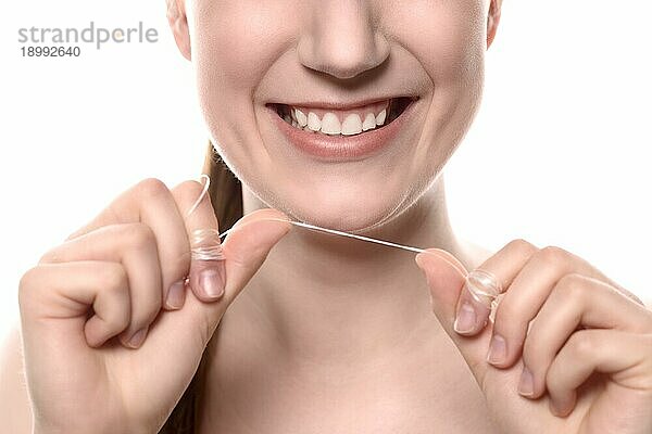 Nahaufnahme des Lächelns einer attraktiven jungen Frau mit gesunden weißen Zähnen  die ein Stück Zahnseide hochhält  in einem Konzept für Mundhygiene  Zahnmedizin und Gesundheitswesen