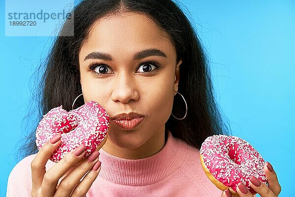 Hungriges hübsches Mädchen ißt Donuts vorblauem Hintergrund. Lecker  Versuchung Essen