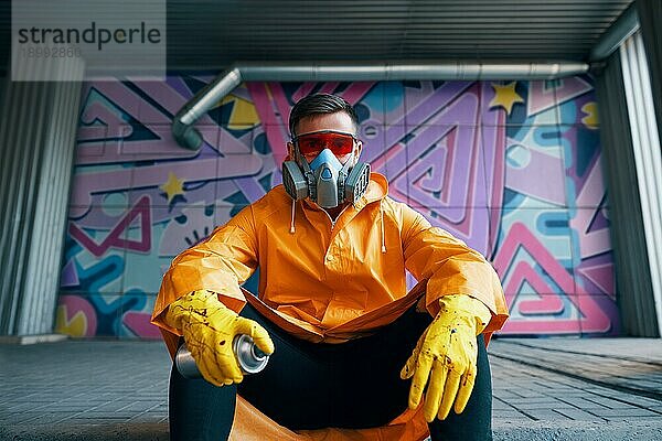 Graffitimaler ruht in der Nähe der Wand mit seinen Gemälden Blick in die Kamera. Street Art Konzept