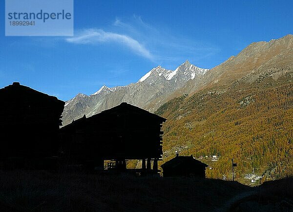 Silhouetten traditioneller Hütten auf Pfeilern  goldener Wald und hoher Berg