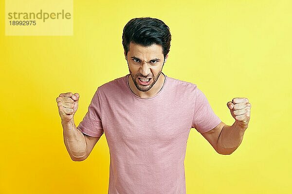 Wütender Mann mit erhobenen Fäusten auf gelbem Hintergrund. Stress Emotionen Konzept