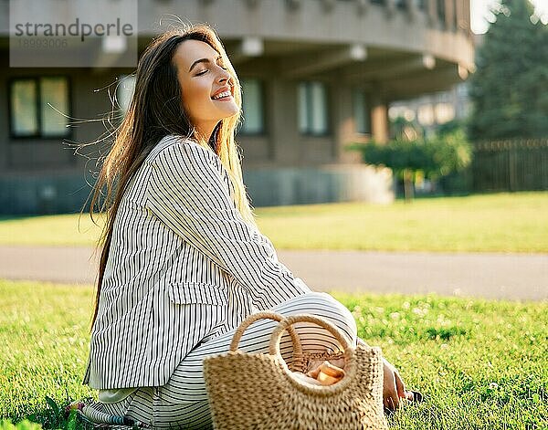 Junge stilvolle Frau entspannen sitzen auf einem Rasen im Stadtpark. Ruhe Konzept