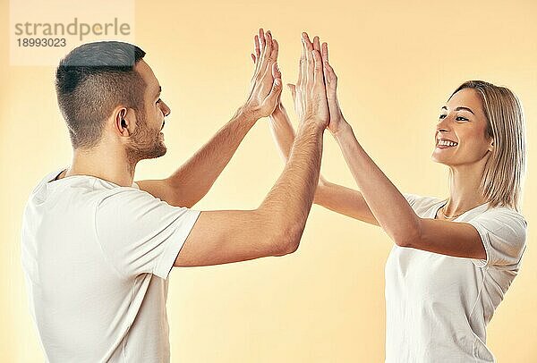 Porträt eines jungen lächelnden Paares  das sich gegenseitig High Five gibt  vor einem Studiohintergrund. Mann und Frau spielen Flammkuchen