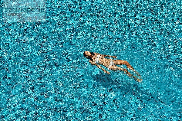 Blick von oben auf junge Frau schwimmen in sauberen türkisfarbenen Wasser im Infinity Pool. Entspannen  Urlaub  Sport Konzept