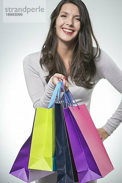 Schöne zufriedene Frau  die eine Reihe von bunten Einkaufstaschen hält und glücklich über ihren erfolgreichen Einkaufsbummel lächelt  slektiver Fokus