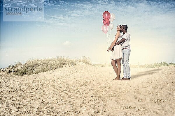 Süßes junges Paar am Strand mit Luftballons an einem sehr sonnigen Tag stehend