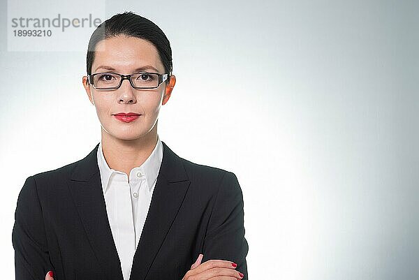 Stilvolle  selbstbewusste Geschäftsfrau mit Brille  die mit verschränkten Armen und ernstem Gesichtsausdruck direkt in die Kamera schaut  Porträt einer Führungskraft oder Managerin mit Kopierbereich