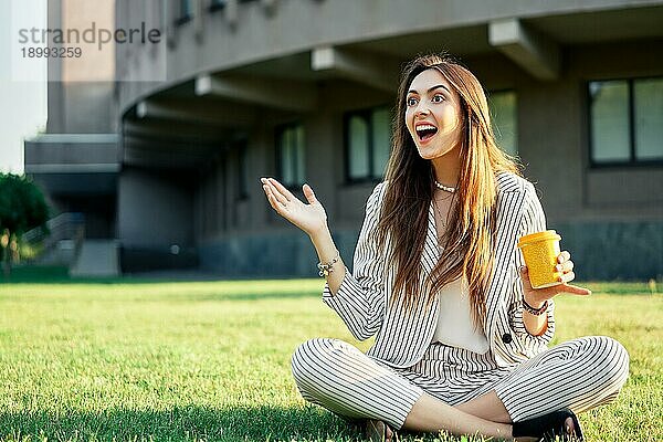 Glücklich und überrascht schöne Frau schauen weg sitzen auf grünem Gras mit Kaffee. Wow Konzept