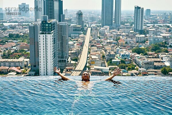 Junger glücklicher Mann entspannt sich am Rande des Swimmingpools auf dem Dach eines Hotels. Sommerurlaub Konzept
