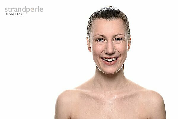 Lächelnde gesunde attraktive Frau mit nackten Schultern und ordentlich zurückgebundenen Haaren in einem Wellness Vitalitäts und Schönheitskonzept vor weißem Hintergrund