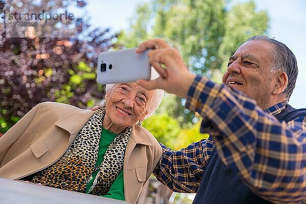 Zwei sehr glückliche ältere Menschen im Garten eines Pflegeheims  die auf das Telefon schauen