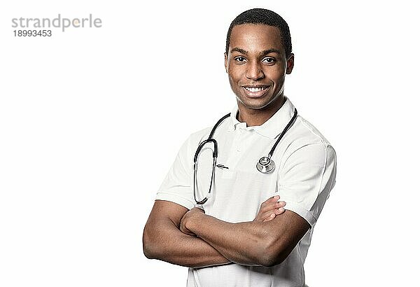 Selbstbewusster afrikanischer Arzt mit einem freundlichen Lächeln  der mit verschränkten Armen und einem Stethoskop um den Hals in die Kamera schaut  Oberkörper vor weißem Hintergrundem Grund